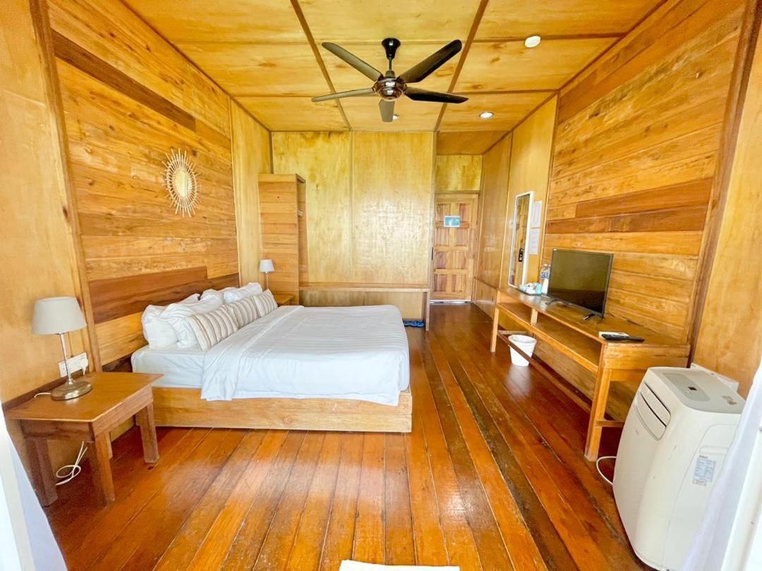 A bright bedroom at Nusakuya Resort featuring a large bed, wooden desk, classic wooden slat walls with varnished timber flooring, and air conditioning.