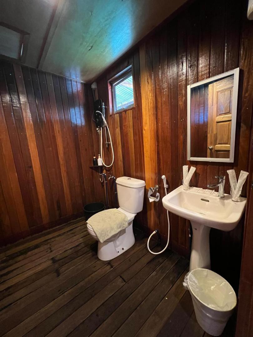 A bright and spacious bathroom at Nusakuya Resort with light wood vanity, large mirror, white ceramic toilet and glass-partitioned electric shower.