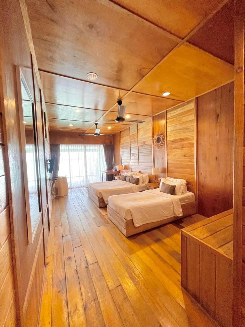A family bedroom at Nusakuya Resort featuring beds facing floor to ceiling glass doors, natural wooden plank walls and air conditioning.