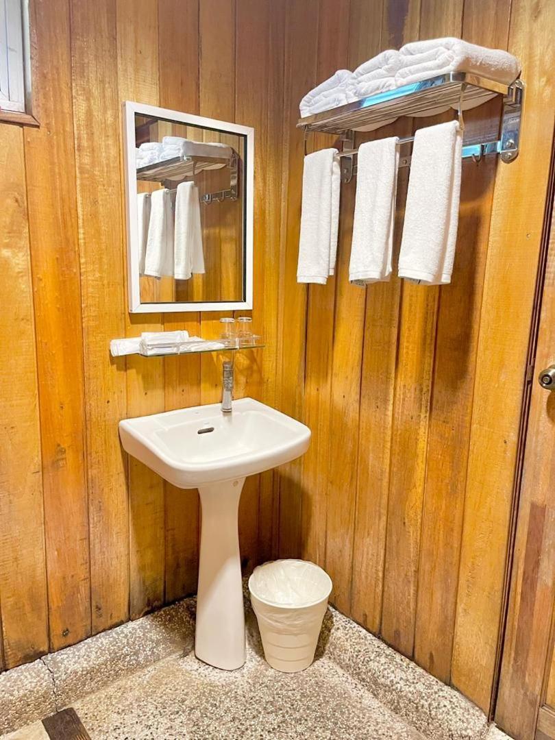 A functional family bathroom at Nusakuya Resort with white ceramic toilet, open electric shower and neutral tiled walls.