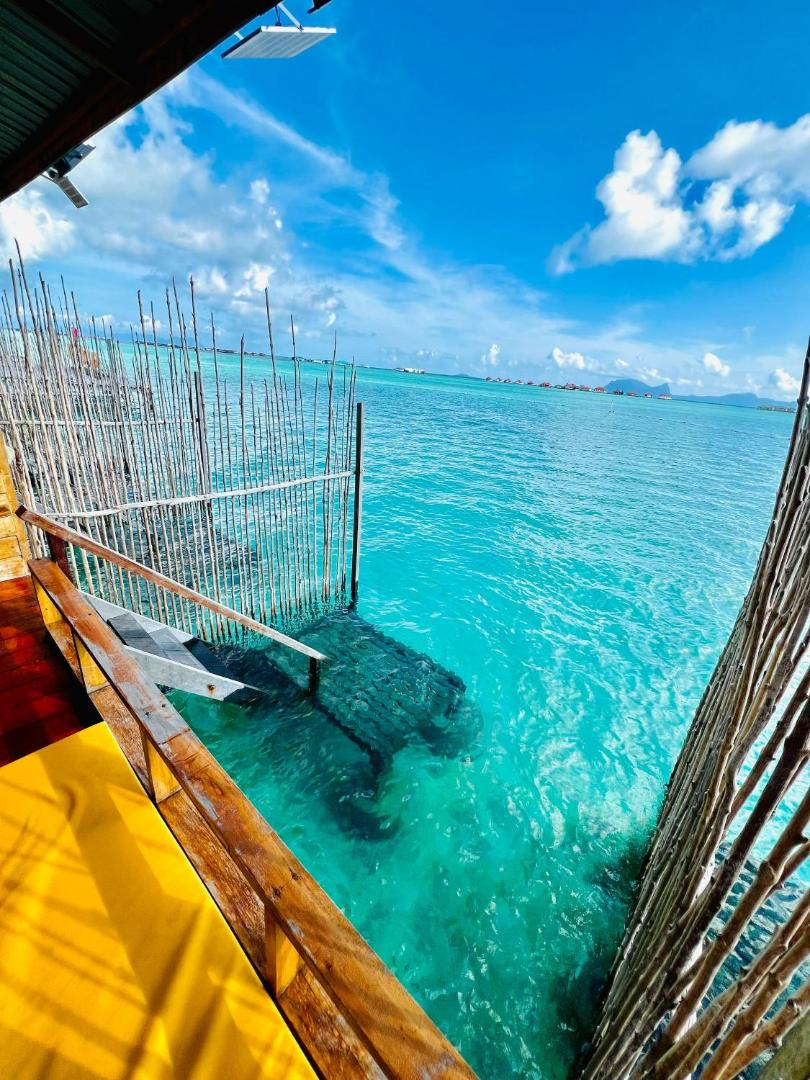 Expansive sun-soaked balcony featuring glass railings and direct wooden stairs to the ocean at Nusakuya Resort.