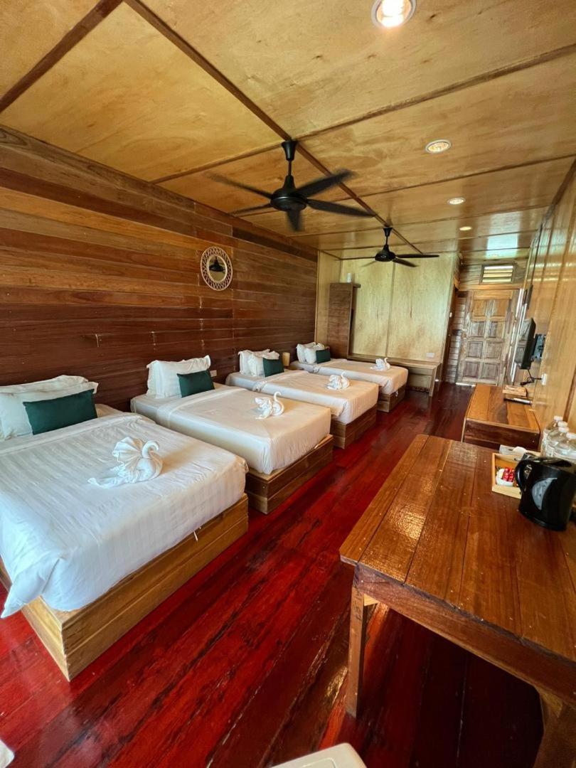 A large bedroom at Nusakuya Resort over the water, presenting four comfortable beds, a desk area, traditional Sabahan wood paneling, gleaming timber floors, and air conditioning.