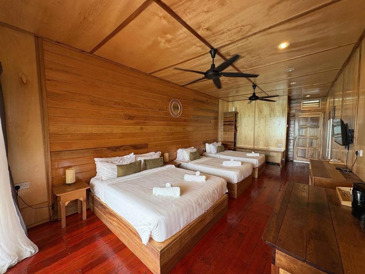 A large bedroom at Nusakuya Resort near Bum Bum Island featuring three beds, authentic wooden walls with glossy timber flooring, and air conditioning.