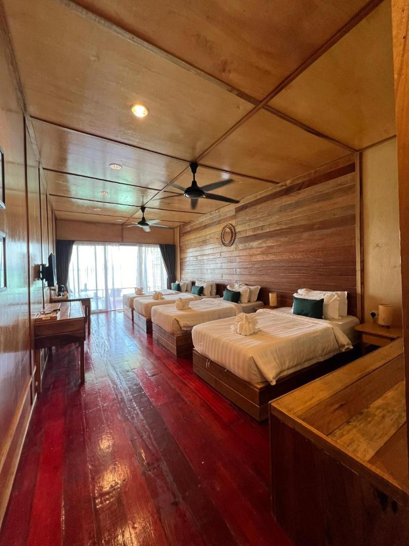 A spacious bedroom at Nusakuya Resort showcasing four beds facing panoramic glass doors, authentic wooden walls, glossy hardwood floors, and air conditioning.