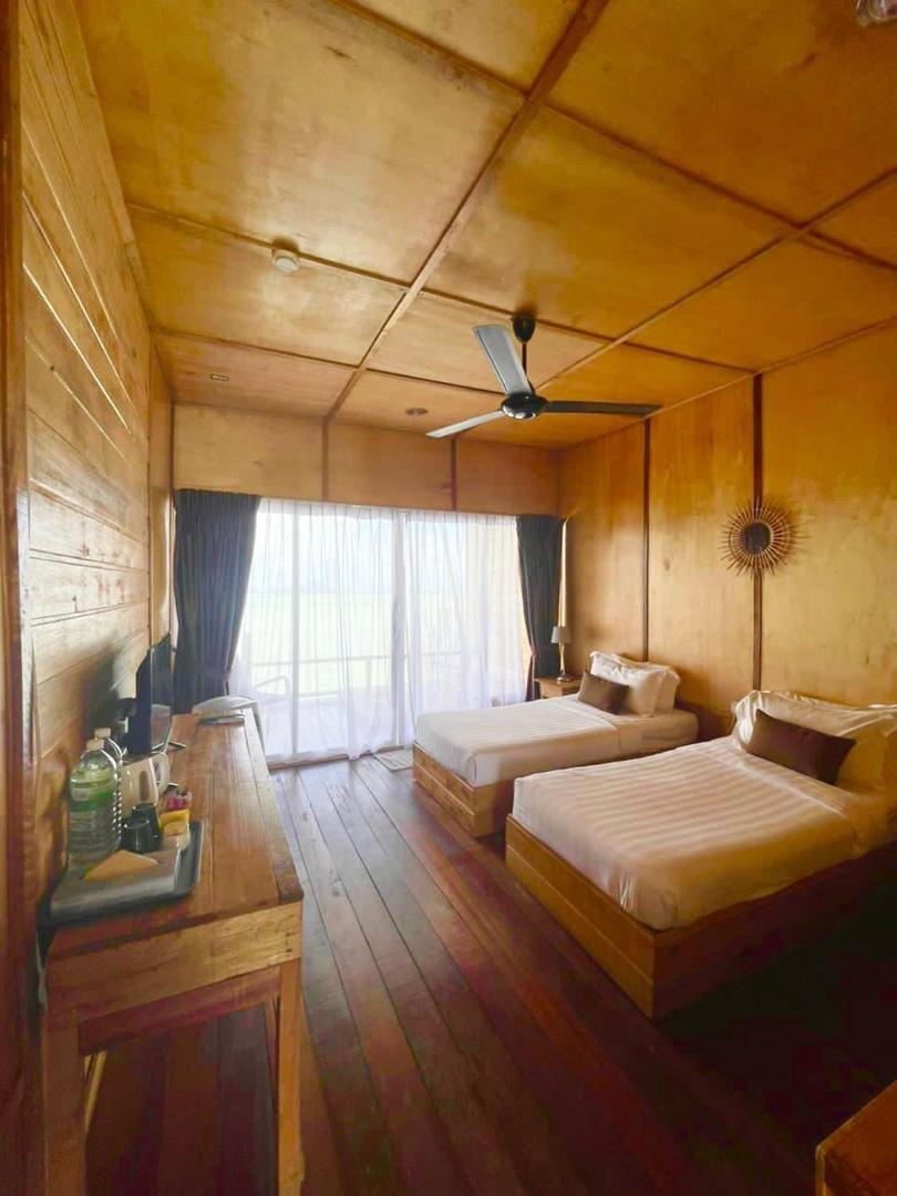 A serene bedroom at Nusakuya Resort in Semporna, offering twin beds facing seamless glass doors, rustic timber walls, smooth wooden boards, and quiet air con.